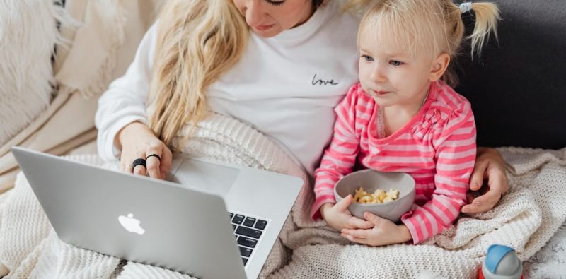 Mother and daughter relaxing on the couch with a laptop and snacks.