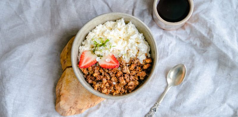 A delicious breakfast bowl with cottage cheese, granola, and strawberries served with black coffee.