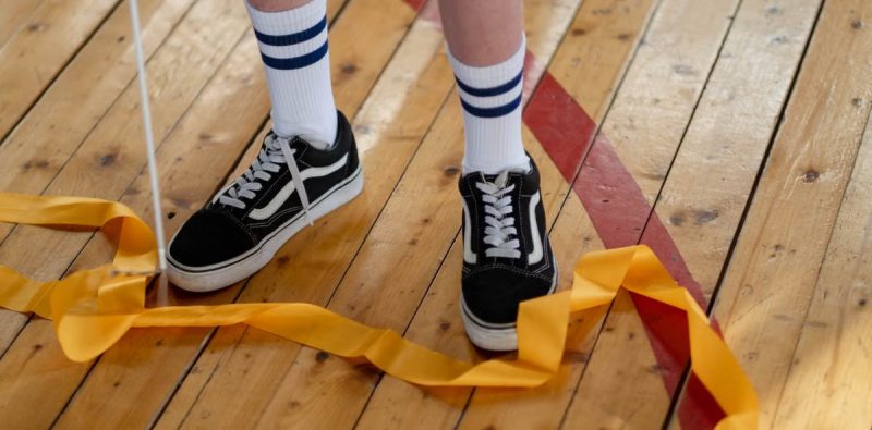 Child's sneakers and gymnastics ribbon on a wooden gym floor; a vibrant, indoor sports setting.